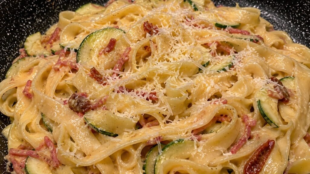 Nahaufnahme von saftiger Carbonar mit Speck und Zucchini in einer Pfanne und mit Pecorino bestreut.