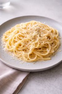 Spaghetti Cacio e Pepe mit Pecorino garniert auf weißem Teller auf weiß gedecktem Tisch