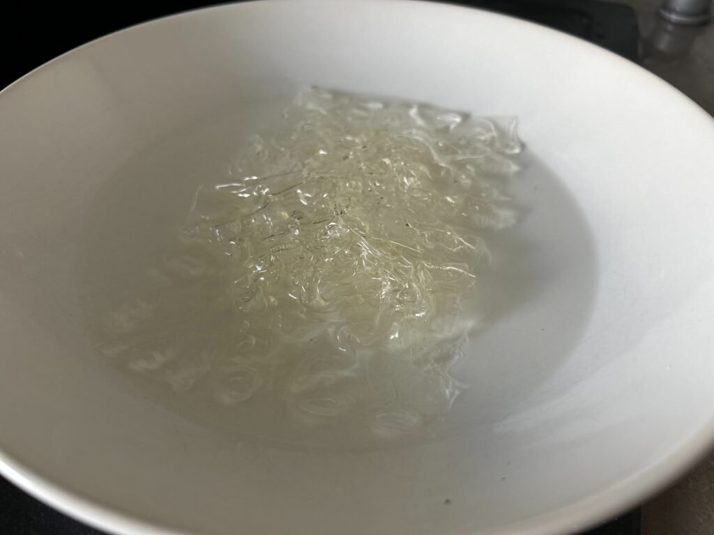 Gelatine wird in einem weißen Teller in kaltem Wasser aufgequellt