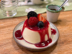 Gestürzte Panna Cotta mit Beerenspiegel und und garniert mit Früchten auf einem gedeckten Holztisch