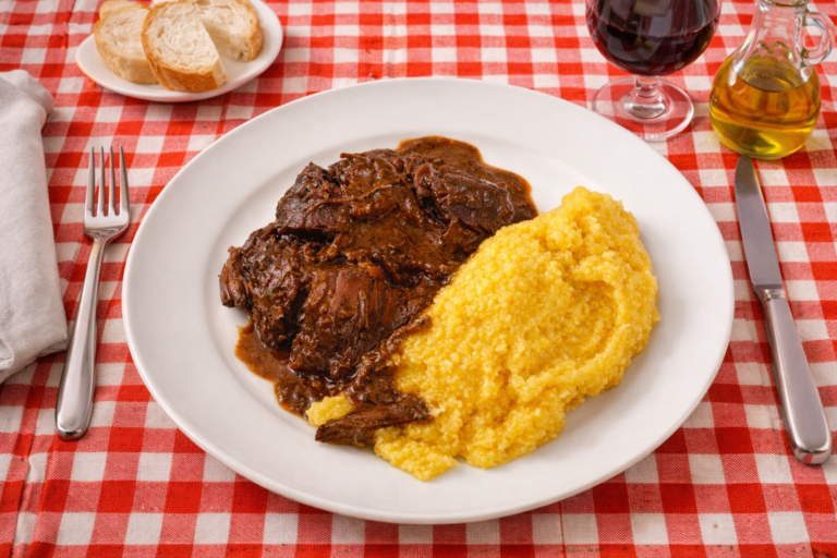 Rinderschmorgericht mit Polenta auf weißem Teller rustikal italienisch gedecktem Tisch