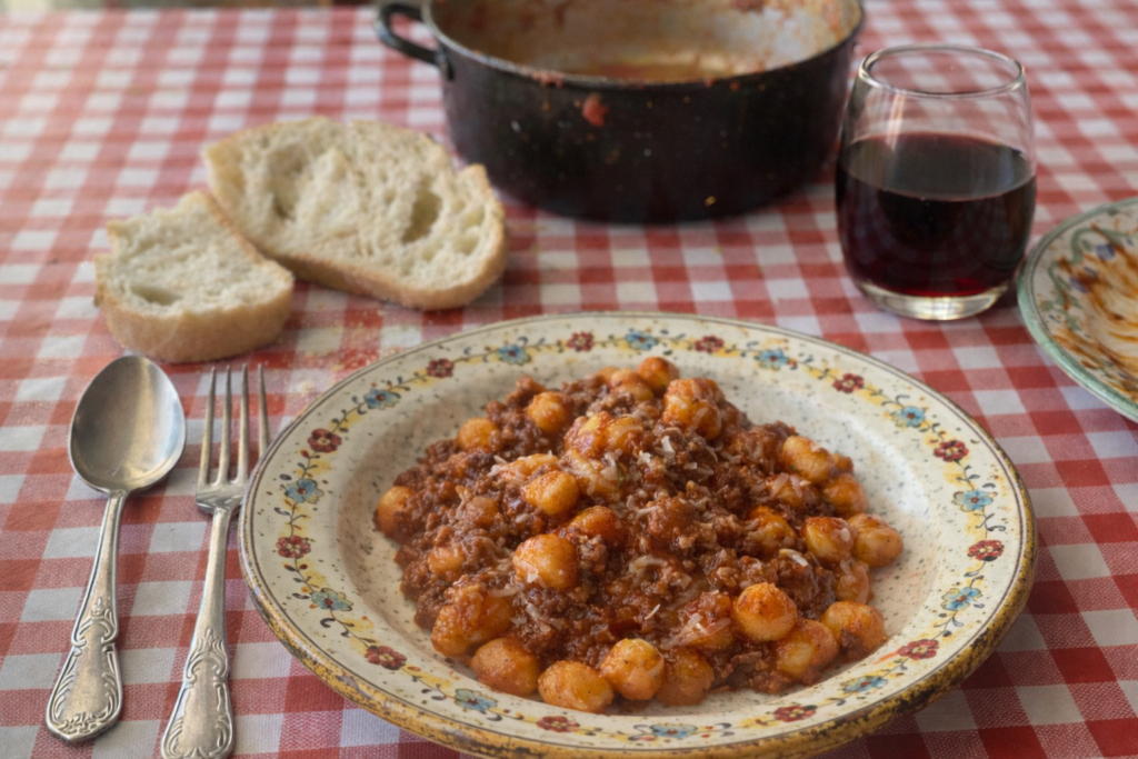 Rustikal gedeckter Tisch mit einem Teller voll Gnocchi mit Hackfleischsauce
