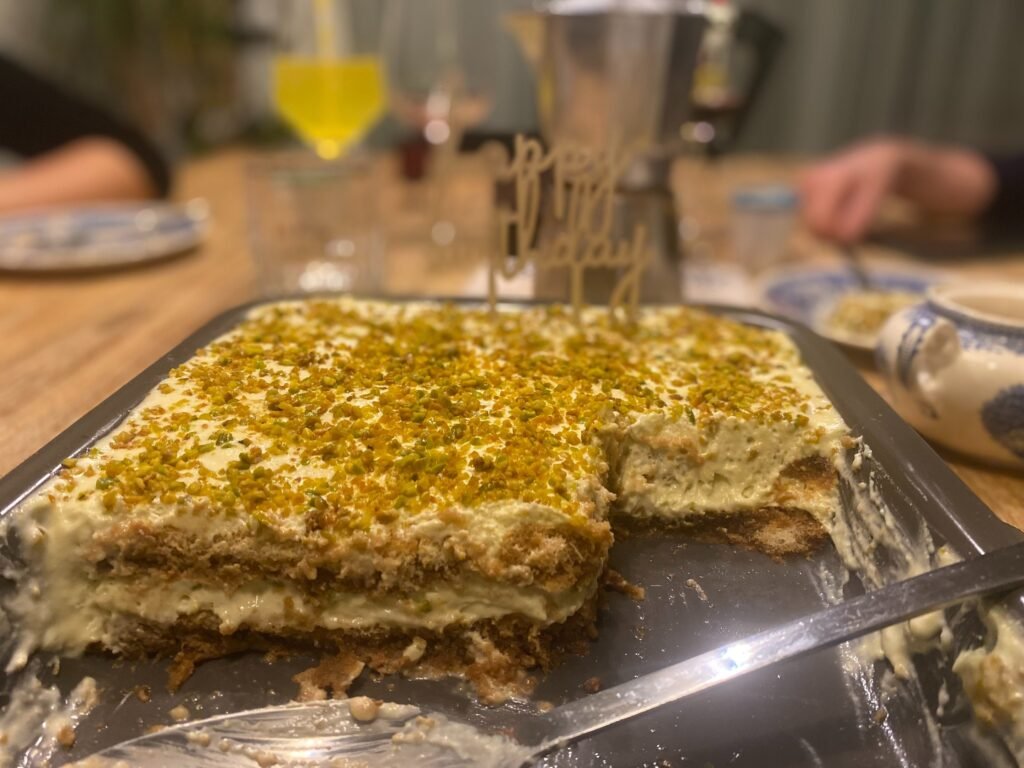 angeschnittenes cremiges Pistazientiramisu auf einem reichlich gedeckten Tisch