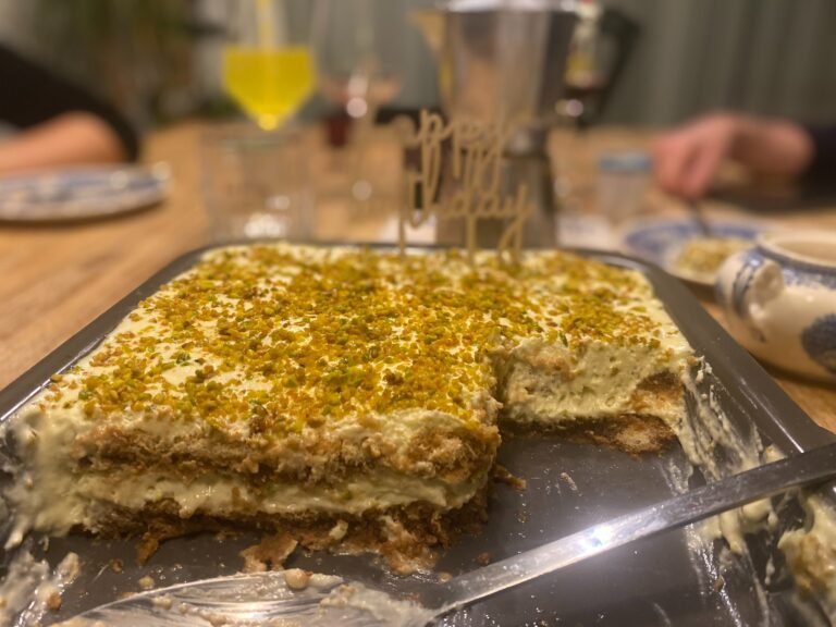 angeschnittenes cremiges Pistazientiramisu auf einem reichlich gedeckten Tisch