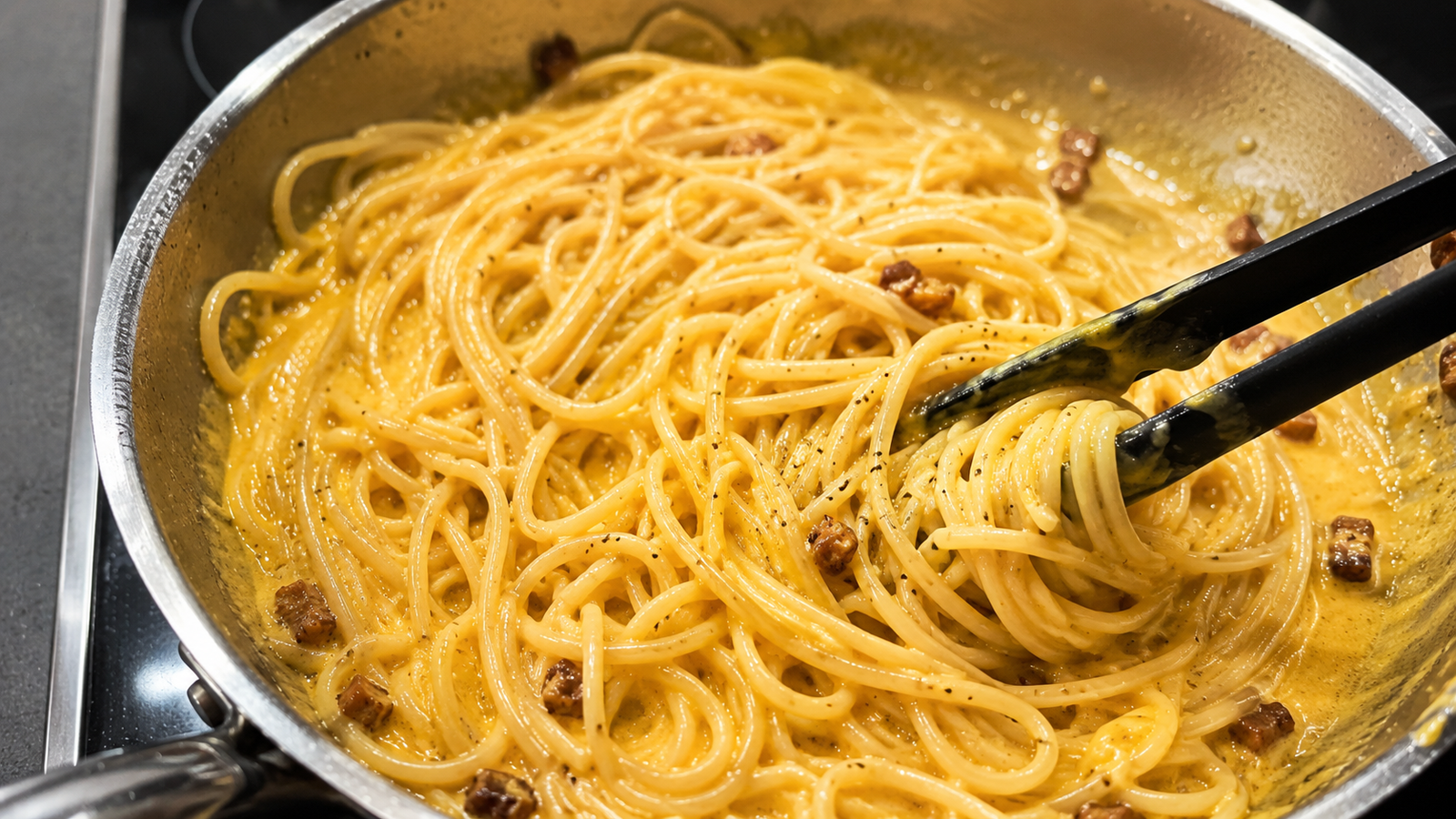 Cremige Carbo-Creme wird in einer Pfanne in die Nudeln eingerührt