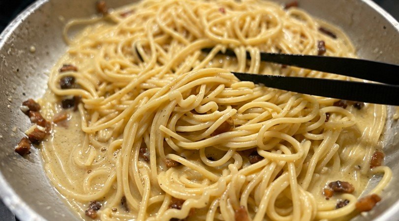 Spaghetti werden in Edelstahlpfanne geschwenkt