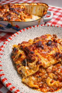 cremige Lasagne auf einem Teller angerichtet mit einer Auflaufform voll Lasagne im Hintergrund