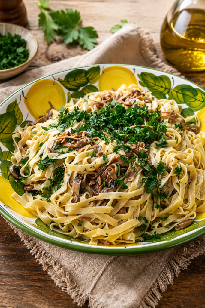 Cremige Tagliatelle ai Porcini mit gebratenen Steinpilzen und frisch geriebenem Parmesan auf rustikalem Keramikteller.
