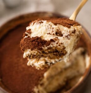 cremiges Tiramisu wird mit einem Löffel aus einer Tonschale mit Kakao bestreuten Tiramisu gehoben