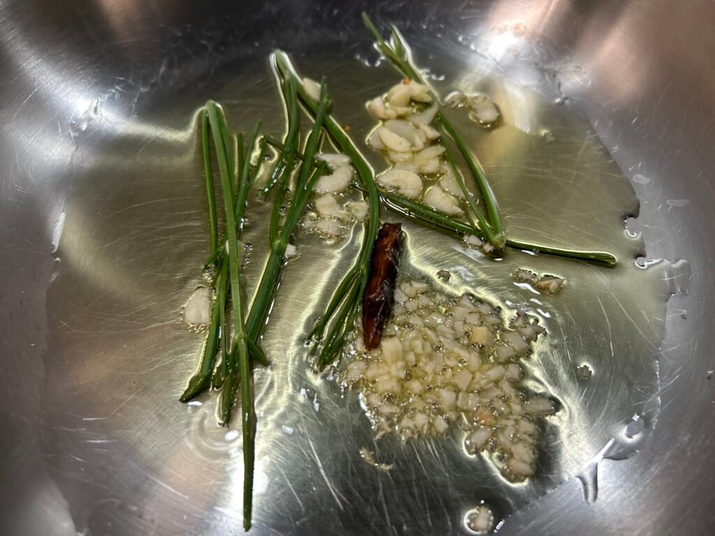 noblauch Peperoncino und Petersilienstängel langsam in Olivenöl für Spaghetti Aglio e Olio e Peperoncino aromatisieren