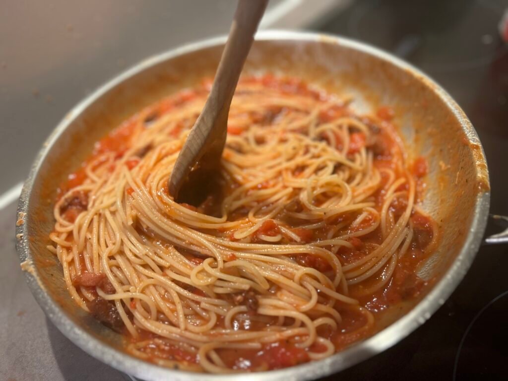 Tomatensauce wird mit Spaghetti vermengt
