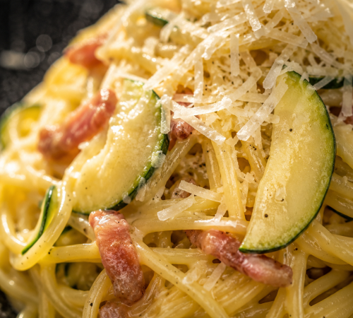 Authentische Linguine Carbonara mit Zucchini und Guanciale auf rustikalem italienischem Tisch.
