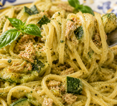 Cremige Pasta mit Zucchini und Thunfisch wird auf dem Teller auf eine Gabel gerollt