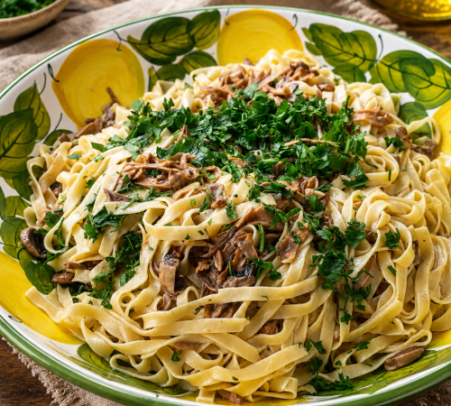 Cremige Tagliatelle ai Porcini mit gebratenen Steinpilzen und frisch geriebenem Parmesan auf rustikalem Keramikteller.