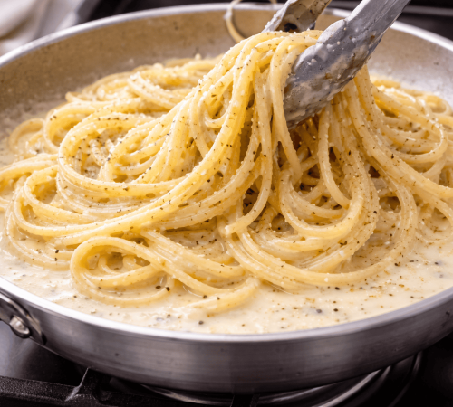 Speaghetti werden in einer Pfanne mit cremiger Käsesauce vermengt