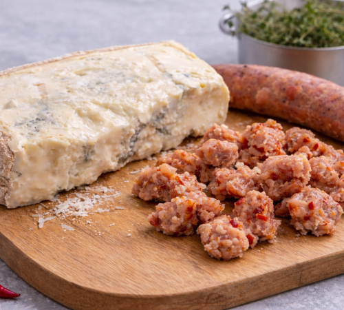 Gezupfte Salsiccia, ein Stück Gorgonzola und eine komplette Salsiccia auf einem Holzbrett im Hintergrund ein Topf mit Thymian